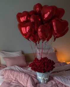 a bunch of red heart balloons in a vase on a bed with pink sheets and pillows