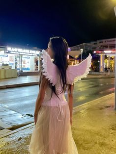 a girl in a pink dress is standing on the street with her wings spread out