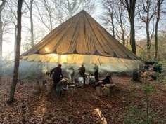 a group of people sitting around a fire pit in the woods under a large tent