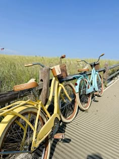 two bicycles parked next to each other on the side of a wooden fence in front of tall grass