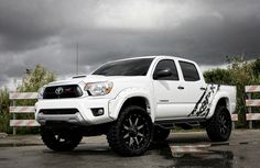 a white toyota truck parked in a parking lot with dark clouds above it and grass behind it