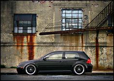 a black car is parked in front of an old building with rusted metal stairs