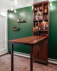 a room with green walls and a wooden table in front of a book shelf filled with liquor bottles