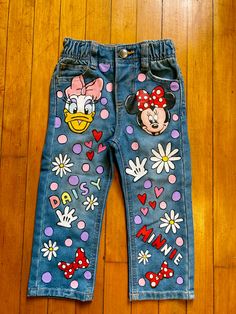 a pair of jeans with mickey and minnie mouse patches on them sitting on a wooden floor