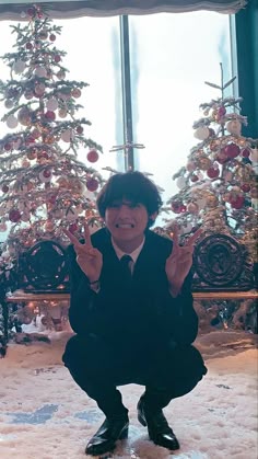 a man kneeling in front of a christmas tree giving the peace sign with his hands