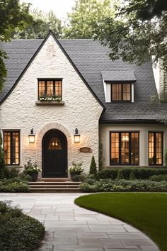 a white brick house with black windows and lights on the front door is surrounded by greenery