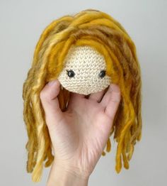 a hand holding up a knitted doll with yellow dreadlocks