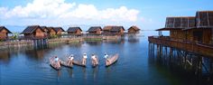 several people on small wooden boats in the water near houses and piers with thatched roofs