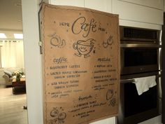 a coffee menu hanging on the wall in a kitchen with stainless steel oven and microwave