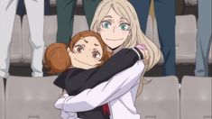 two anime characters hugging each other in front of people with their arms around one another