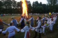 a group of people standing around a fire in the middle of a field next to trees