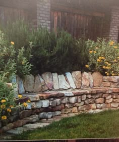 there is a stone wall with flowers growing out of it and grass in the foreground