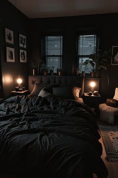 a dark bedroom with two windows and a bed covered in black sheets, pillows and blankets