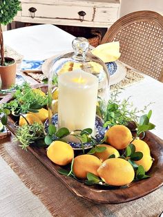 a candle is lit on a tray with lemons and greenery in front of a dining room table