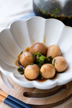 a white bowl filled with food next to chopsticks on top of a wooden table