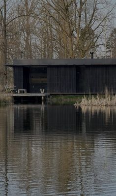 a black house sitting on top of a lake next to a lush green forest filled with trees