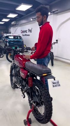 a man standing next to a red motorcycle in a garage with other motorcycles behind him