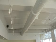 an empty room with lots of white pipes hanging from the ceiling and lights on the ceiling