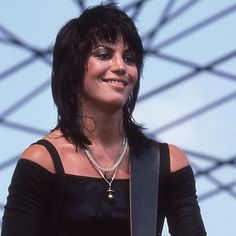 a woman with black hair and piercings holding a guitar in her right hand while standing next to a fence