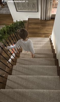 a toddler walking up the stairs in a house with carpeted floors and wooden handrails