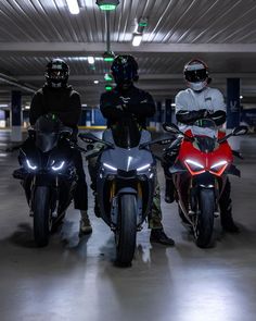 three people on motor bikes in a parking garage with one person wearing a helmet and the other standing behind them