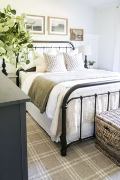a bed with white sheets and pillows in a bedroom next to a basket full of plants