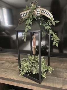 a black lantern with greenery in it on a wooden table