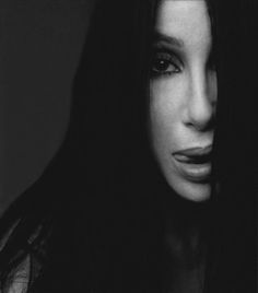 a black and white photo of a woman's face with long dark hair, looking at the camera