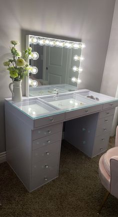 a white vanity with lights on it and a pink chair