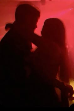 two people standing next to each other in front of a red light with their arms around one another