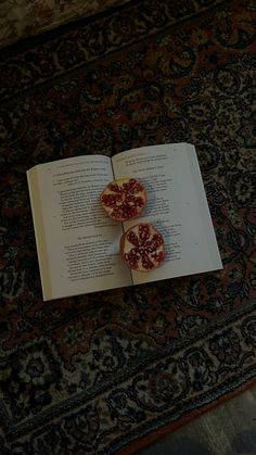 an open book with two pieces of fruit on top of it sitting on a rug