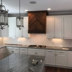 a kitchen with white cabinets and marble counter tops, chandelier hanging from the ceiling