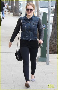 a woman in black leggings and denim jacket walking down the street with her handbag