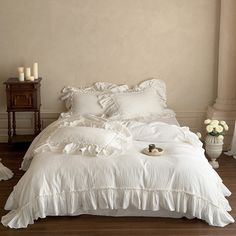 a white bed with ruffles and pillows in a room next to a window