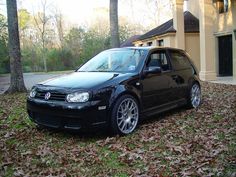 a black car parked in front of a house with leaves on the ground around it