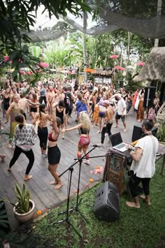 a large group of people dancing on a wooden deck in the middle of a park