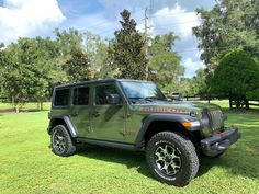 a green jeep parked on top of a lush green field with trees in the background