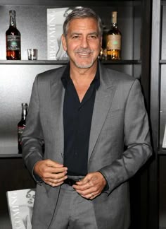 a man in a gray suit and black shirt standing next to shelves with liquor bottles