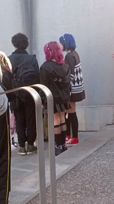 some people are waiting for their luggage at the bus stop and one is wearing pink hair