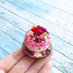 a hand holding a tiny cake with pink icing and sprinkles