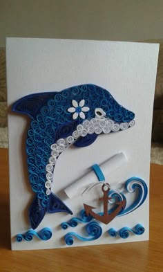 a handmade card with a dolphin and an anchor on the front, sitting on top of a wooden table