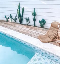 a wooden chair sitting next to a swimming pool with cactus plants on the side of it