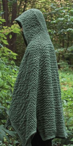 a person wearing a green knitted hooded cloak in the woods