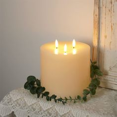 three lit candles sitting on top of a lace covered table cloth next to an old window