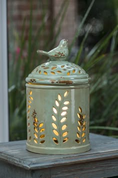 a bird sitting on top of a green jar with lights inside it and a window in the background