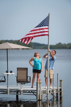 a man and woman standing on a dock with an american flag in front of them