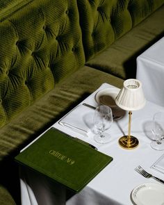 the table is set with wine glasses, silverware and a green velvet sofa behind it