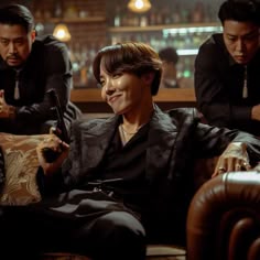 three men sitting on a couch looking at their cell phones in front of the camera