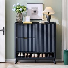 a black cabinet with shoes on it next to a lamp and vase filled with flowers