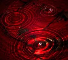 a red light reflecting on the surface of water with circles and bubbles in it's center